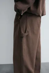 Pantalón negro de corte amplio, confeccionado en tejido de algodón con efecto lavado. Presenta bolsillos frontales, traseros de parche, tira multifunción y bolsillos laterales en las perneras. Cuenta con cierre frontal con cremallera y botón.