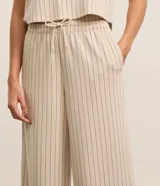Conjunto deportivo de dos piezas color beige con finas rayas verticales negras. Incluye un chaleco corto con cuello en V y un pantalón palazzo con cintura elástica ajustable.