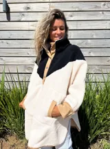 Buzo tipo poncho de polar color crudo con bloque superior en negro y detalles en beige.