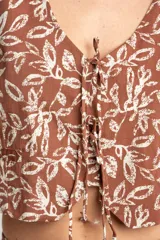 Chaleco marrón con estampado de hojas blancas, escote en V y lazo ajustable en el centro.