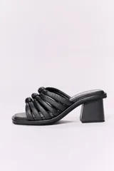 Sandalia de cuero negro con tiras de cuero trenzadas y anudadas en el empeine. Tiene taco cuadrado de 6 cm de altura.