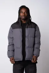 Campera puffer gris con la parte superior negra, cierre frontal y cuello alto.