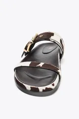 Sandalias planas con estampado animal print de piel con pelo, cierre mediante hebilla metalizada y punta redonda.