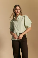 Camisa blanca de manga corta con volumen en los hombros, cuello camisero y cierre frontal con botones dorados.