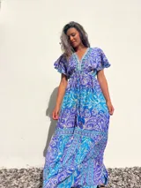 Vestido largo de seda con estampado paisley en tonos turquesa, azul y blanco. Tiene escote en V, mangas cortas con volados y talle imperio con cordón ajustable.