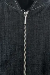 Cazadora bomber de denim color gris oscuro, con cuello redondo, cierre frontal con cremallera metálica, bolsillos laterales y mangas largas con puños elásticos.