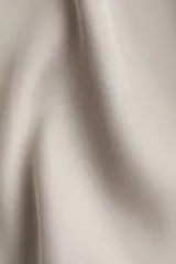 Blusa de manga larga color gris claro o beige pálido, con acabado satinado y cuello clásico que forma un escote en V profundo con cierre de botones frontales.