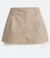 Minifalda color beige de sarga con cintura baja, trabillas, cierre con corchete y cremallera, y forro de bolsillo aparente.