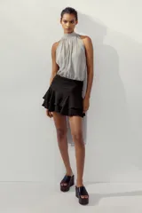 Falda pantalón corta de color negro, con tiro medio, detalle de pliegues en la cintura y volantes en el ruedo. Cierre lateral con cremallera.