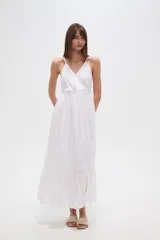 Vestido largo blanco de algodón con broderie, escote en V cruzado y breteles finos. Presenta un corte entallado en la cintura con elástico y falda fluida con tajo lateral.