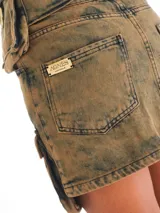 Minifalda de denim color marrón con efecto desgastado, bolsillos laterales y traseros, y parche con logo de la marca en la parte posterior.