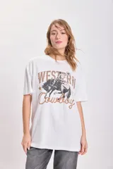 Remera blanca de corte amplio con estampa de un cowboy montando un caballo y la frase "Western Cowboy" en letras marrones y estilo cuerda. 