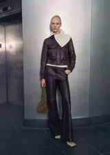 Chaqueta bomber de cuero color marrón oscuro con cuello camisero y cierre frontal con cremallera y botones a presión. Tiene terminaciones elásticas en puños y cintura, y dos bolsillos laterales.