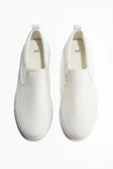 Zapatillas slip-on blancas de lona con elásticos laterales, cuello acolchado y tirador trasero.