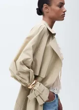 Trench beige de algodón con cuello con solapa, trabillas, manga larga con trabillas, cierre delantero, solapas con muesca, dos bolsillos laterales, diseño recto, cinturón desmontable y forro interior.
