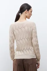 Sweater de punto color beige claro, con escote bote y tejido calado con patrón ondulado. Es de manga larga y corte recto.