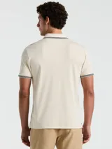 Polo color crema con cuello clásico, mangas cortas y logo bordado en el pecho. Presenta detalles de doble línea en cuello y mangas.