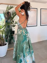 Vestido largo de tela fluida, color verde esmeralda con estampado abstracto en tonos turquesa y detalles dorados. Diseño asimétrico con un solo tirante tejido en el hombro.