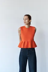 Top tejido de punto color naranja, de cuello redondo y sin mangas. Tiene corte ajustado en el torso y peplum en la cintura.