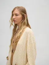 Cardigan largo color crema con detalles en color camel en el borde de los bolsillos, en el borde de los botones y en los puños. Tiene cuello en V y cierre con botones.
