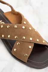 Sandalias bajas de cuero color marrón con tiras cruzadas y tachas doradas.