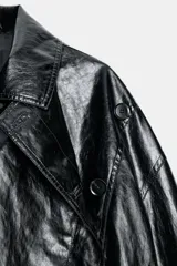 Chaqueta de Zara Woman Collection en tejido con acabado brillante efecto cuero. Presenta cuello solapa, manga larga con trabillas ajustables, bolsillos delanteros y cierre frontal con botones ocultos bajo solapa.