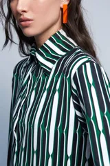 Camisa de manga larga con cuello clásico y estampado de líneas verticales en blanco, negro y verde. Corte holgado, mangas con pinzas laterales y puños anchos.