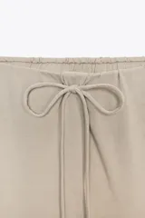 Pantalón de algodón color beige, de corte amplio y tiro alto, con cintura elástica ajustable con cordones y bolsillos laterales.