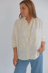Camisa color crudo con bordado de flores, cuello mao con volados y mangas largas con puños elásticos.