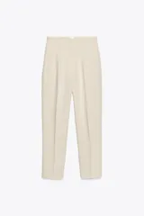 Pantalón de vestir color crema, de tiro alto, corte recto y largo cropped. Presenta bolsillos laterales de ojal y cierre frontal con cremallera, botón interior y gancho metálico.