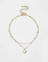 Collar corto dorado de doble cadena, una con cuentas pequeñas y otra con bolitas. Dije redondo esmaltado en blanco con diseño de sol y estrellas.