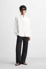Camisa color arena de lino con cuello abotonado, manga larga con puños abotonados, corte regular y bajo con aberturas laterales.