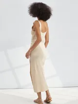 Vestido midi beige ajustado al cuerpo, sin mangas y con escote redondo. Presenta un frunce lateral que genera un drapeado y una abertura alta en la pierna.