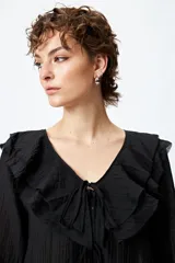 Blusa blanca de gasa con escote en V y volados en el cuello y las mangas largas. Se ata con lazos finos al frente.