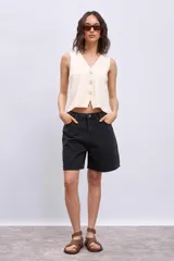 Chaleco de tejido punto color crema, sin mangas, con escote en V y cierre frontal con tres botones.