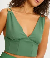 Blusa cropped color verde bosque, con escote en V profundo, tirantes dobles finos y estructura tipo corsé con costuras verticales en el frente.