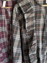 Camisa de tela escocesa liviana, color gris oscuro con líneas en blanco, azul marino y salmón. Presenta un diseño con volados verticales en el frente y mangas abullonadas.