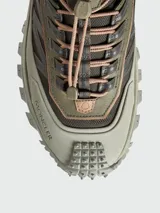 Zapatillas de trail running Moncler modelo Trailgrip GTX, color verde oliva y marrón topo. Presentan un sistema de cordones elásticos con tope, puntera y suela robusta con tacos prominentes para tracción.