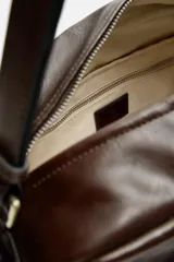 Bandolera marrón de piel envejecida con compartimento principal con cremallera, bolsillo interior plano y con cremallera, dos bolsillos frontales con botón a presión, dos bolsillos laterales con cremallera y asa de hombro ajustable de piel.
