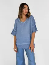 Blusa celeste de lino con escote en V y mangas cortas con volados. Tiene terminaciones desflecadas en el escote, mangas y ruedo.