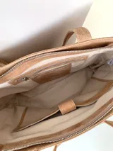 Cartera tipo tote de cuero graneado color negro, con textura uniforme y suave al tacto. Tiene manijas de 55 cm, bolsillo frontal con broche imantado, bolsillo trasero con cierre metálico, cierre principal metálico, forro interior y tres bolsillos internos (uno con cierre, uno plaqué y uno tipo sobre con solapa y botón).