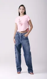 Pantalón de jean de corte ancho, color azul medio, con lavado gastado y estampados de caligrafía oriental en color blanco a lo largo de las piernas.