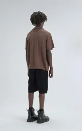 Camisa de tejido de punto color café, manga corta y cuello polo con botones frontales. Presenta un patrón calado de espiga o chevron.