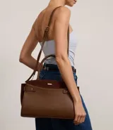 Cartera satchel mediana color marrón, confeccionada en cuero sintético con detalles en gamuza. Cuenta con asas medianas, cierre de cremallera y detalles metálicos dorados. Incluye correa extraíble y regulable.