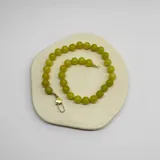 Collar elaborado con bolitas de Jade Limón de 10 mm de diámetro, ensartadas con hilo color salmón que forma nuditos separadores. Cuenta con un broche tipo langosta y terminaciones en acero con baño de oro.