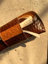 Estuche para lentes color borgoña con textura símil cocodrilo y cierre con broche a presión.