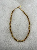 Collar corto de perlas doradas con hilo de seda azul marino y cierre de mosquetón dorado con cadena de extensión.