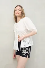 Short de denim negro con bordado floral blanco, bolsillos funcionales y bajo con pequeña abertura lateral.