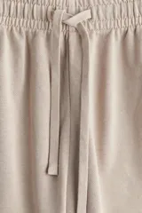 Pantalón deportivo color beige de corte holgado, confeccionado en felpa de algodón liviano con efecto lavado. Cuenta con cintura elástica fruncida, cordón para ajustar, bolsillos laterales discretos y bajos sin rematar.