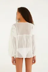 Blusa blanca con diseño cutwork, escote en V con cordones para anudar, mangas largas con leve frunce y puños ajustables.